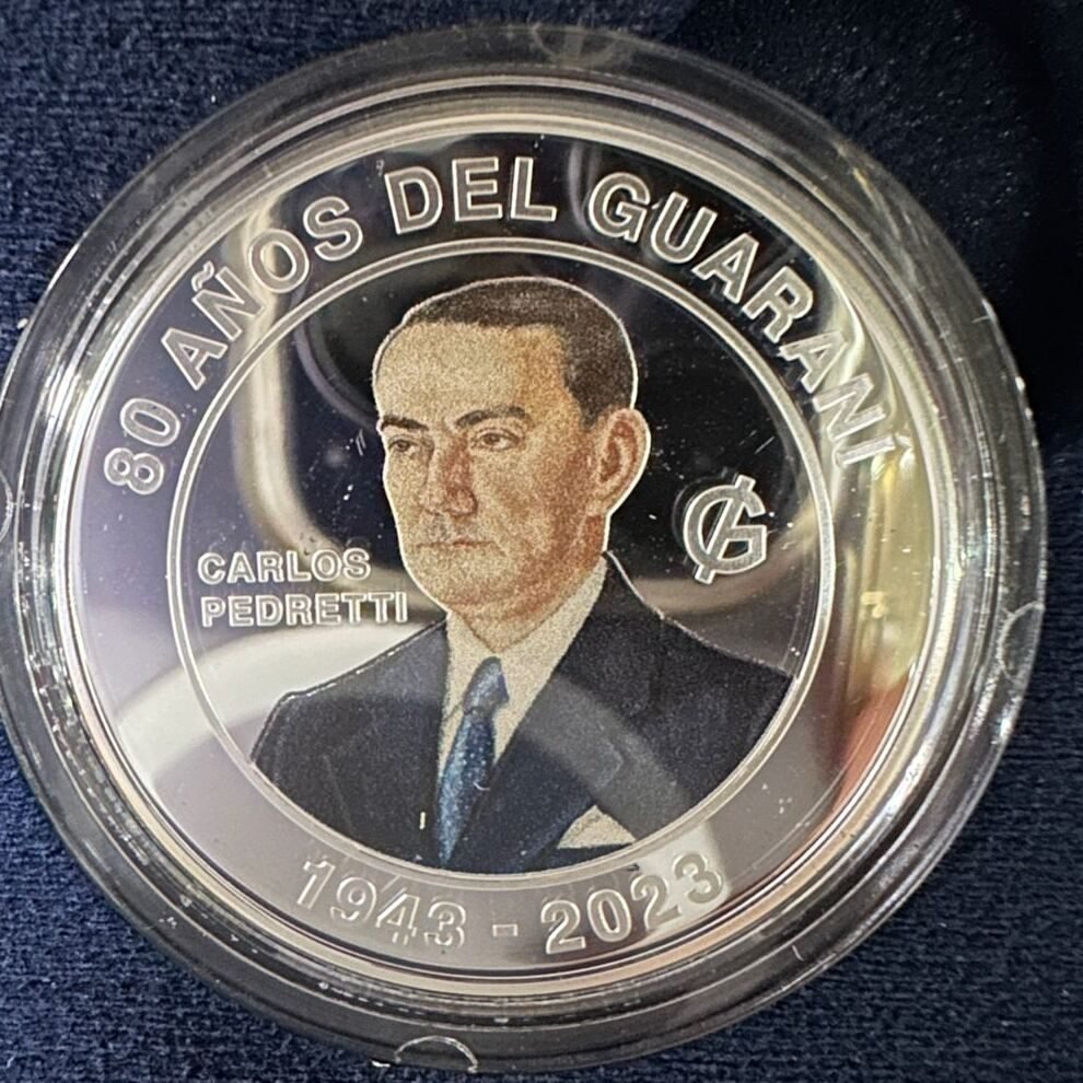 Moneda conmemorativa del Banco Central del Paraguay (2023): «80 AÑOS DEL GUARANÍ», busto y nombre «CARLOS PEDRETTI», «1943 - 2023». La leyenda no dice que haya